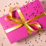 Regalo personalizado rectangular envuelto en papel color rosa y asegurado con cinta dorada en España