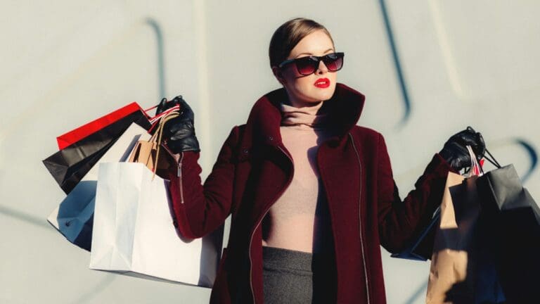 Mujer vestida a la moda con lentes oscuros, sostiene bolsas de compra con ropa para mujer en España