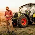 Imagen de un agricultor eligiendo maquinaria agrícola en un campo, con equipos como tractores y sembradoras.