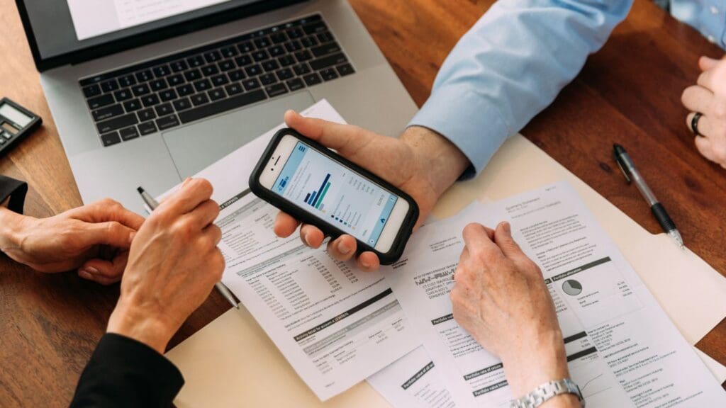 Persona revisando documentos financieros en un escritorio con gráficos, laptop y calculadora, representando una gestión financiera eficiente para empresas.