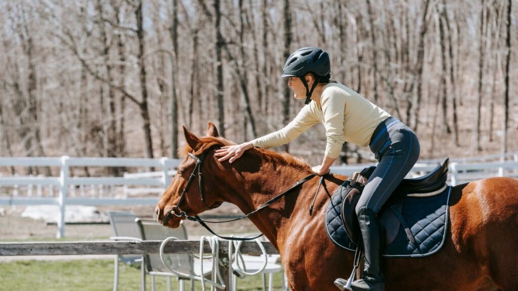 Persona aprendiendo equitación. Jinete principiante montando a caballo con casco de seguridad en un entorno natural durante una clase de equitación.