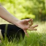 Persona practicando yoga en posición de meditación al aire libre, rodeada de naturaleza, simbolizando bienestar físico y mental para todas las etapas de la vida.