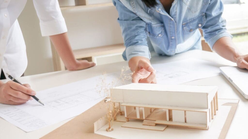 Arquitectos trabajando en diseños innovadores con una maqueta y planos arquitectónicos sobre un escritorio.