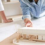 Arquitectos trabajando en diseños innovadores con una maqueta y planos arquitectónicos sobre un escritorio.