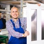 Trabajador sosteniendo una puerta moderna de PVC en un taller de fabricación. Materiales duraderos y eficientes energéticamente para hogares y negocios.