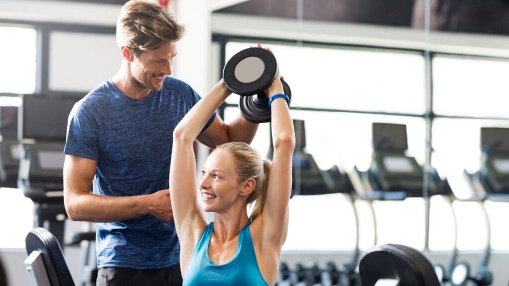 Mujer entrenando con un entrenador personal en un gimnasio moderno, realizando ejercicios funcionales para mejorar su fuerza y bienestar.