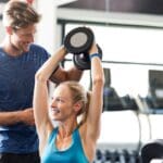 Mujer entrenando con un entrenador personal en un gimnasio moderno, realizando ejercicios funcionales para mejorar su fuerza y bienestar.