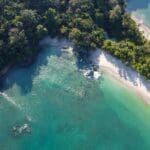 A stunning view of Santa Teresa Beach with surfers catching waves under a vibrant sunset, showcasing the natural beauty and popular activities in this Costa Rican paradise.