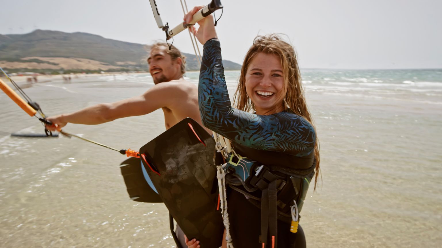 Personas disfrutando del surf y kitesurf en una playa de aguas cristalinas de Fuerteventura, rodeadas de un paisaje natural espectacular ideal para deportes acuáticos.