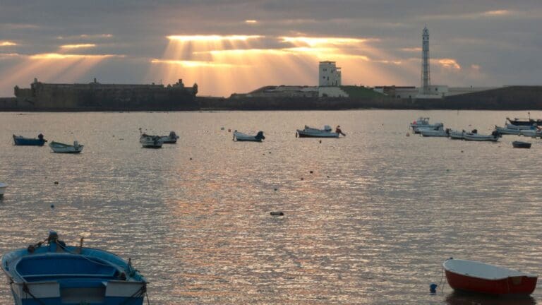 Atardecer en la Bahía de Cádiz visto desde un barco. Cielo teñido de colores cálidos reflejados en el agua, ideal para un paseo exclusivo.