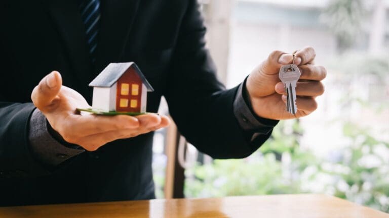 Broker ofreciendo una casa en miniatura y llaves, representando servicios hipotecarios y oportunidades de compra de vivienda.