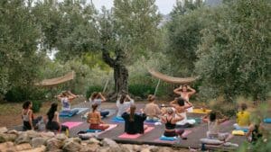 Persona practicando yoga al aire libre en un entorno natural rodeado de árboles y montañas, simbolizando conexión, relajación y bienestar.