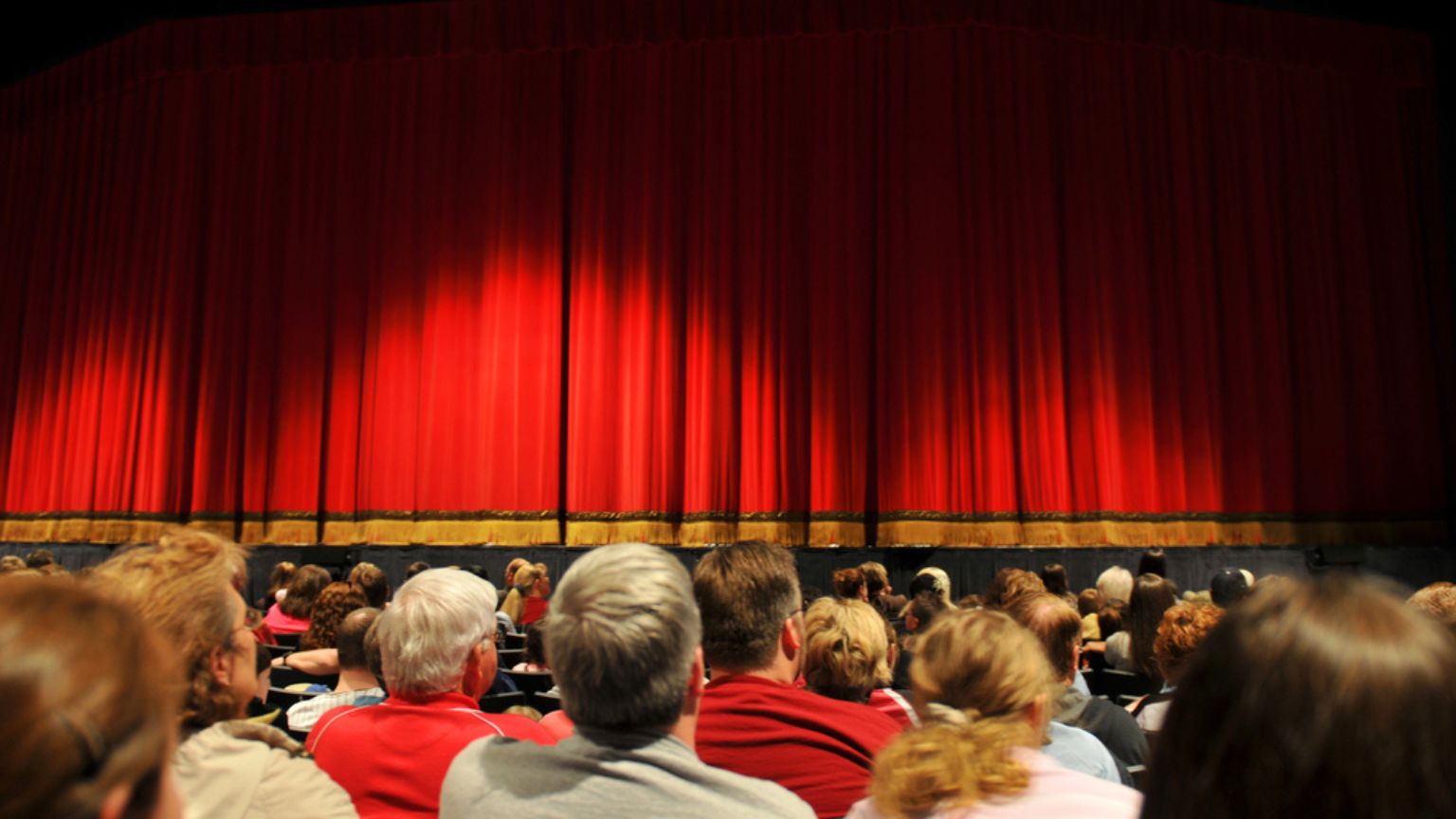 Grupo de personas disfrutando de una función de teatro, con el auditorio iluminado y la atención centrada en el escenario.