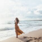 A free-spirited woman wearing a flowy bohemian dress, walking confidently through a natural setting. The earthy tones, delicate embroidery, and relaxed silhouette highlight the effortless elegance and individuality of bohemian fashion.