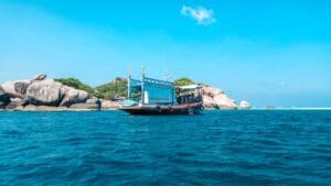 Barco turístico navegando en aguas cristalinas cerca de una isla rocosa con exuberante vegetación bajo un cielo azul despejado.