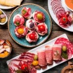 Assorted traditional Spanish tapas including patatas bravas, served on a rustic wooden table at a Madrid terrace