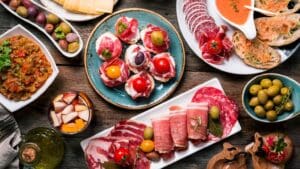 Assorted traditional Spanish tapas including patatas bravas, served on a rustic wooden table at a Madrid terrace