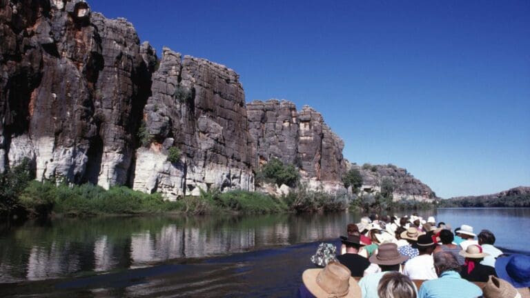 Grupo de turistas navegando por un río rodeado de imponentes acantilados rocosos bajo un cielo azul despejado en un paisaje natural impresionante.