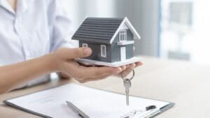 Manos sosteniendo una maqueta de casa con llaves, simbolizando la compra, venta o alquiler de propiedades inmobiliarias.