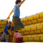 Niños jugando y saltando en un inflable amarillo durante una fiesta infantil al aire libre, disfrutando de una actividad segura y divertida.