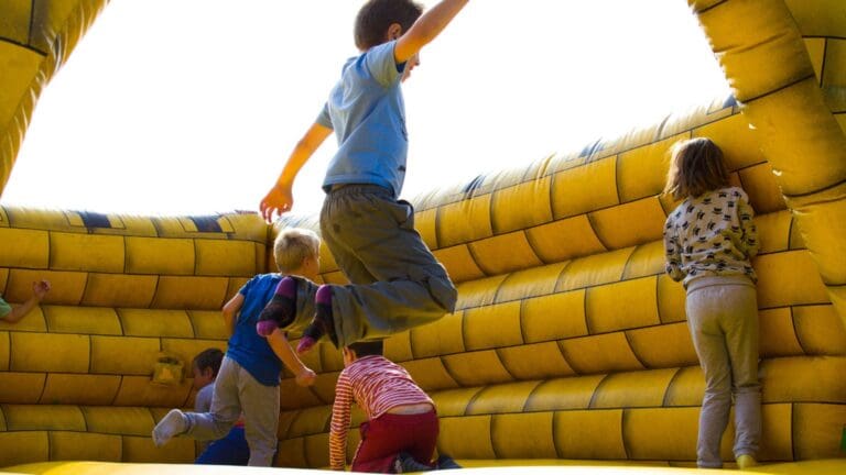 Niños jugando y saltando en un inflable amarillo durante una fiesta infantil al aire libre, disfrutando de una actividad segura y divertida.