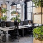 Oficina moderna con mobiliario reutilizado y plantas naturales, diseño sostenible y luz natural abundante.