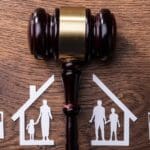 Ilustración de custodia compartida con mazo judicial y figuras recortadas de familia dividida en dos hogares, simbolizando decisión legal en divorcio