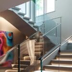 Escalera interior con barandilla de cristal transparente en diseño moderno, que aporta luz natural y seguridad al hogar.