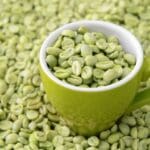 Granos de café verde sin tostar en un cuenco con fondo natural, símbolo de bebida saludable y antioxidante.