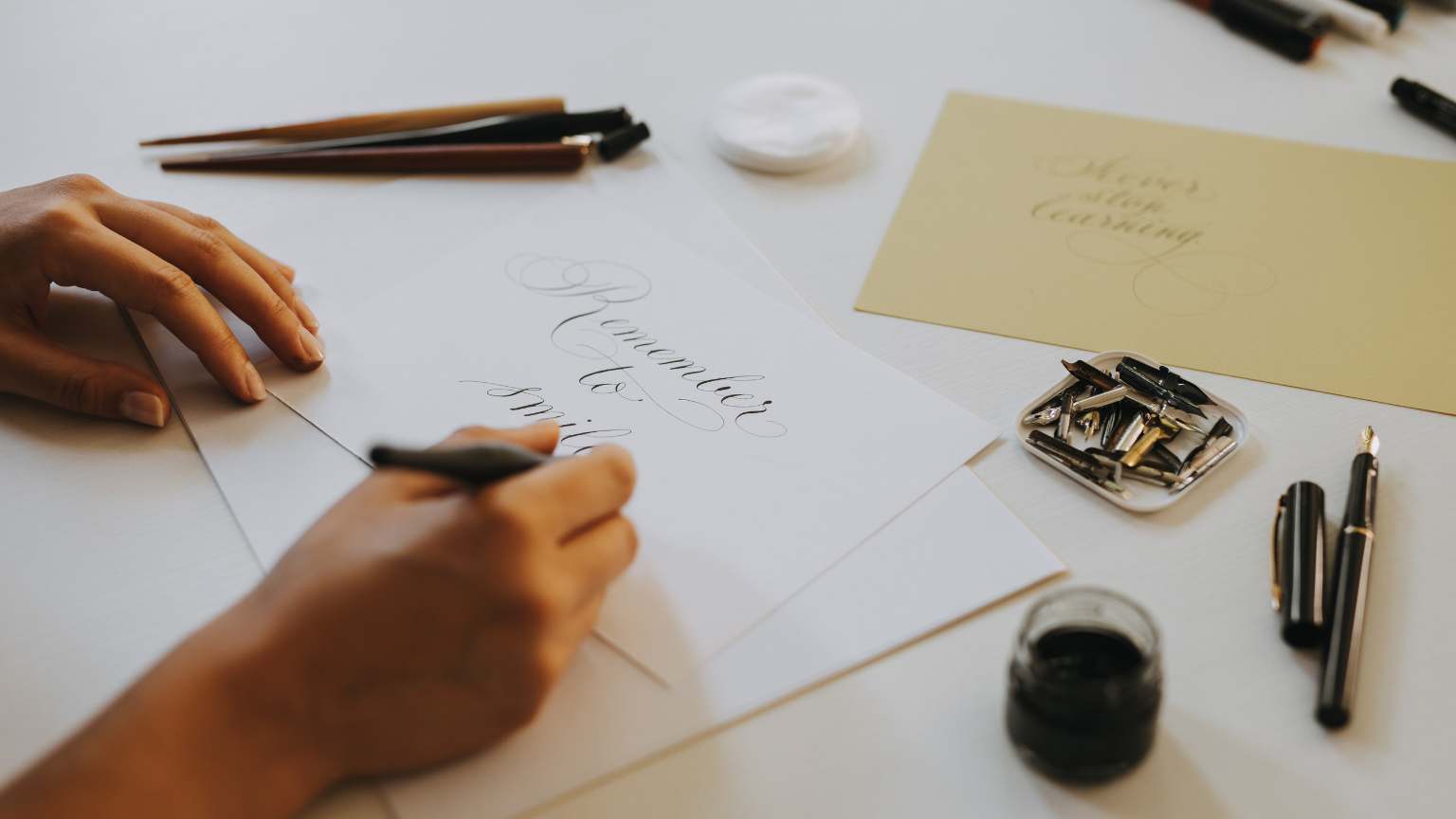 Calígrafo profesional escribiendo a mano con tinta negra sobre papel, representando la elegancia del diseño caligráfico tradicional