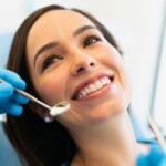 Paciente sonriente en clínica dental después de tratamiento completo con ortodoncia, implantes y estética dental.
