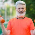 Hombre mayor ejercitándose al aire libre con pesas pequeñas como parte de una rutina integral para mantener la salud física y mental