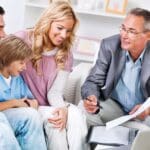 Familia española sonriente recibe asesoramiento sobre seguros de salud y vida con tranquilidad y confianza en una correduría profesional