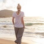 Mujer joven caminando cerca del mar con ropa ecológica de inspiración marina, representando moda sostenible con diseño natural y conciencia ambiental
