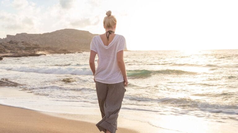 Mujer joven caminando cerca del mar con ropa ecológica de inspiración marina, representando moda sostenible con diseño natural y conciencia ambiental