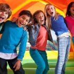 Niños jugando en castillo hinchable durante una fiesta infantil al aire libre con actividades y animación.
