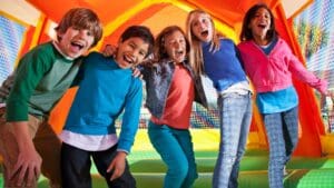 Niños jugando en castillo hinchable durante una fiesta infantil al aire libre con actividades y animación.