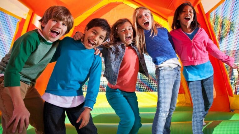 Niños jugando en castillo hinchable durante una fiesta infantil al aire libre con actividades y animación.
