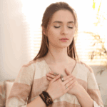 Mujer con los ojos cerrados y las manos sobre el pecho, en un gesto de conexión interior y amor propio, representando la calma y la fuerza del amor incondicional.