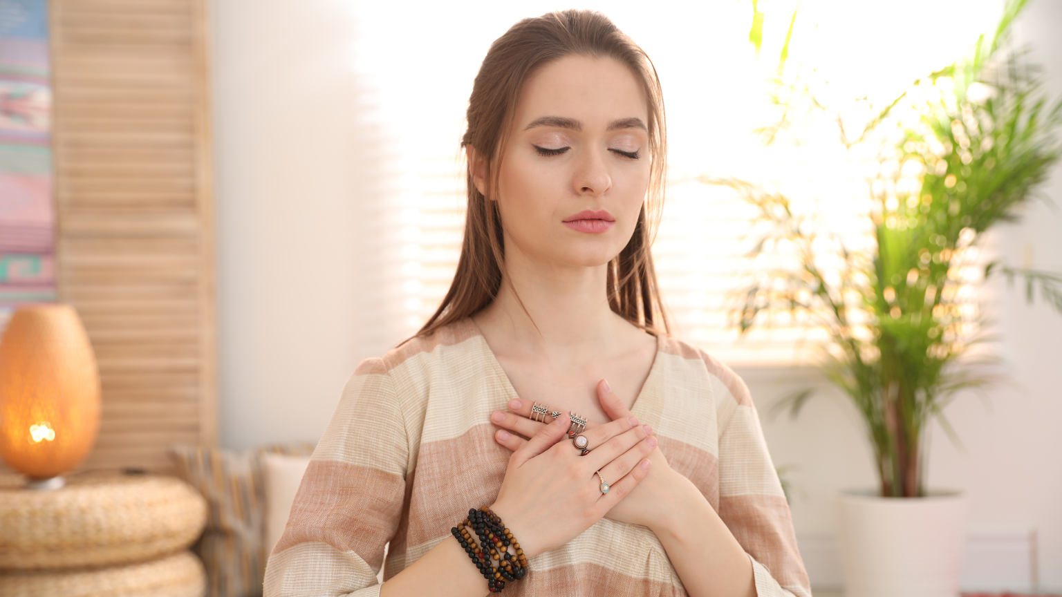 Mujer con los ojos cerrados y las manos sobre el pecho, en un gesto de conexión interior y amor propio, representando la calma y la fuerza del amor incondicional.