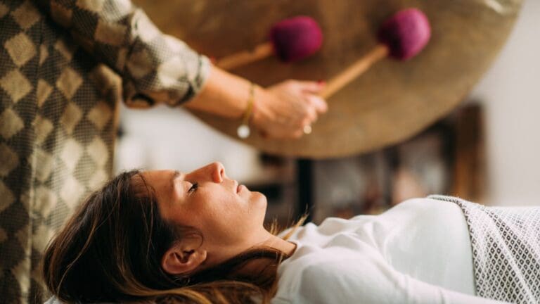 Mujer recibiendo una sesión de terapia de sonido con gong en un espacio de meditación, rodeada de energía vibracional y atmósfera de sanación emocional.