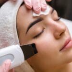 Mujer joven con piel luminosa recibiendo tratamiento facial moderno en centro de estética, representando las tendencias en estética facial para 2025.