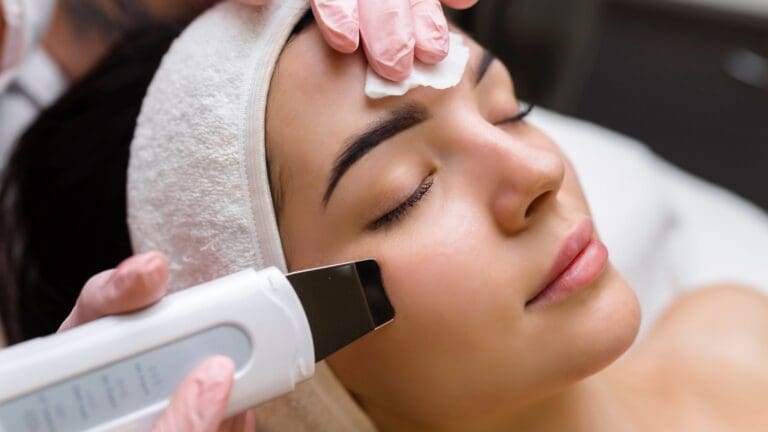 Mujer joven con piel luminosa recibiendo tratamiento facial moderno en centro de estética, representando las tendencias en estética facial para 2025.