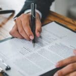 Mano de abogado extranjería revisando y firmando solicitud de nacionalidad española con documentos legales sobre mesa