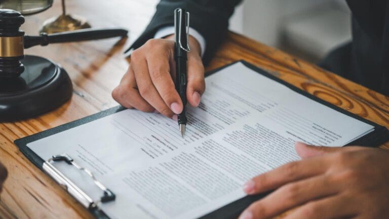 Mano de abogado extranjería revisando y firmando solicitud de nacionalidad española con documentos legales sobre mesa