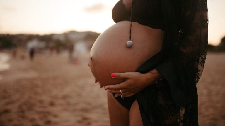 Mujer embarazada en sesión de fotos con luz natural, sonriendo y abrazando su barriga en un entorno emocional y cálido.