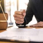 Abogado estampando un sello sobre un documento legal, con balanza de la justicia y libros jurídicos sobre la mesa en una oficina profesional.