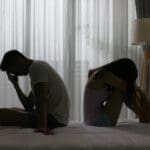 Pareja sentada en la cama enfrentando una ruptura emocional en silencio y tensión
