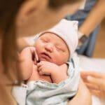 Madre primeriza con su bebé en brazos en casa usando ropa cómoda de maternidad