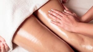 Mano realizando masaje con aceite en piernas femeninas para aliviar la sensación de pesadez y mejorar la circulación.